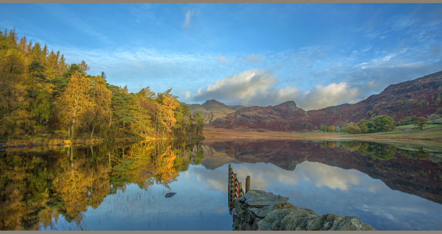 Blea Tarn reflects autumn trees, mountains and sky beyond